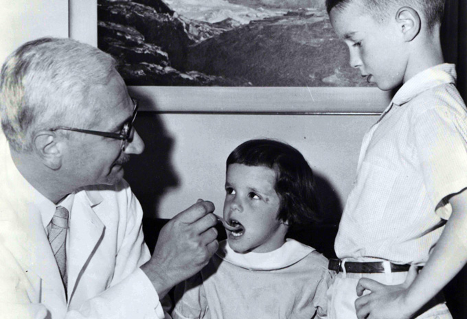 Albert Sabin giving a young child the polio vaccine, while another child waits