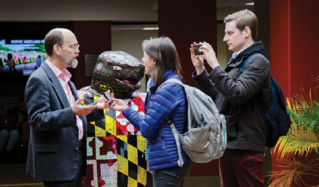 photo of Aimee Cunningham holding a digital recorder as Mike Denison films her interviewing a researcher at the University of Maryland