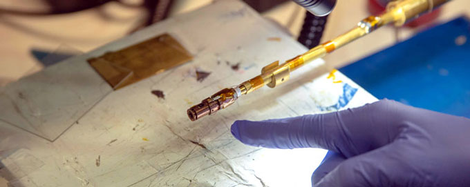 A gloved hand points to a diamond anvil cell in a lab.