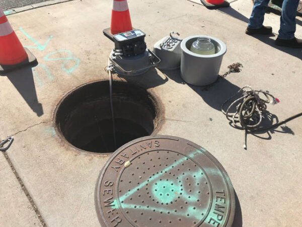 A small automated machine perches at the edge of a maintenance hole, ready to retrieve wastewater samples from the Tempe, Ariz., sewage system.