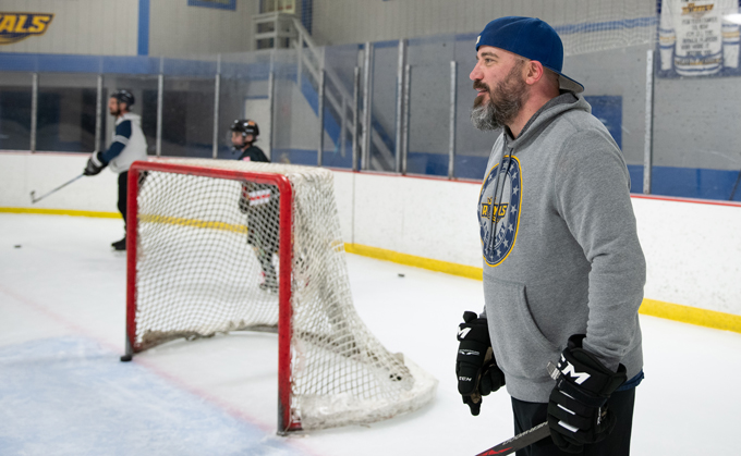 A photo of Jon Nelson standing on an ice rink next to a red hockey goal.