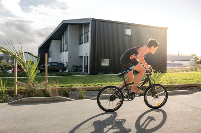 A young boy on a bicycle rides pass a house.