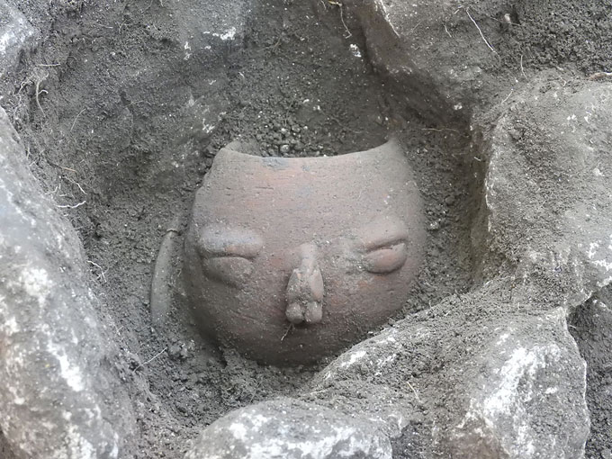 A partially excavated pot with a face decoration from Caracol