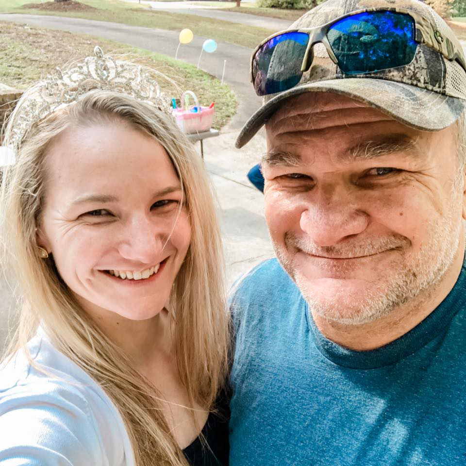 A selfie-style photograph of Carla Wiggins (left) with her father, Carlton “PeeWee” Gautney Jr. (right). They both smile in the direction of the camera.